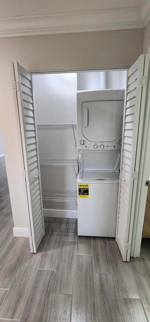 washroom with crown molding, stacked washing maching and dryer, and hardwood / wood-style flooring