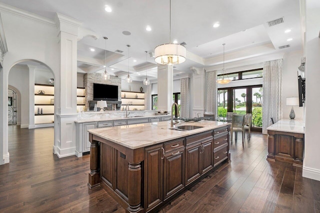 kitchen featuring light stone countertops, dark brown cabinets, sink, hanging light fixtures, and an island with sink