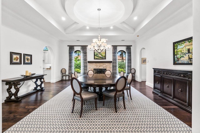 dining area featuring dark hardwood / wood-style flooring, an inviting chandelier, a stone fireplace, and coffered ceiling