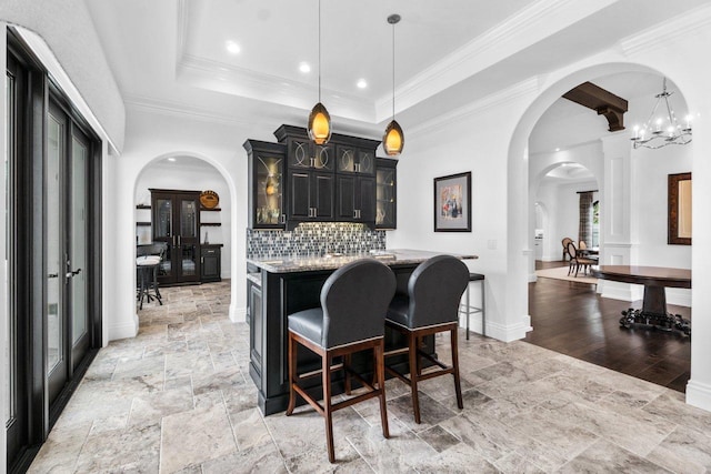 kitchen featuring light stone countertops, backsplash, a tray ceiling, pendant lighting, and a center island