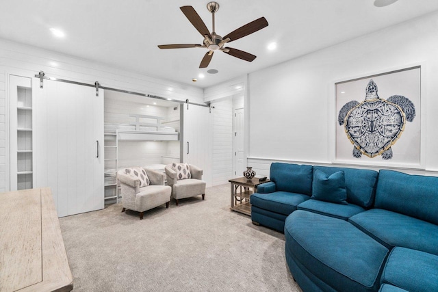 living room with a barn door, ceiling fan, and light colored carpet