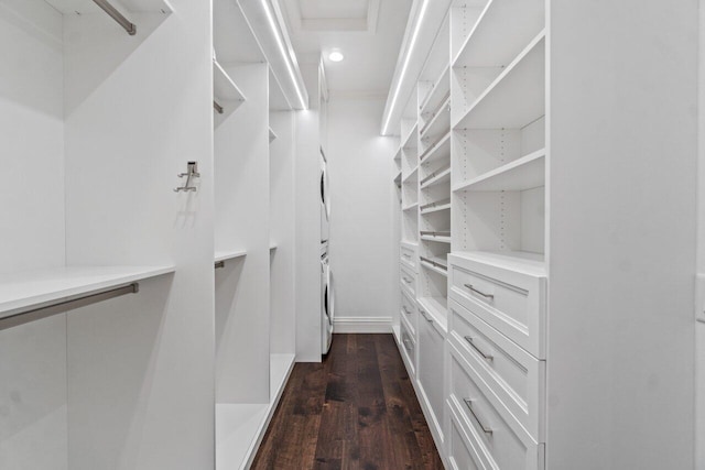 walk in closet with dark wood-type flooring and stacked washing maching and dryer