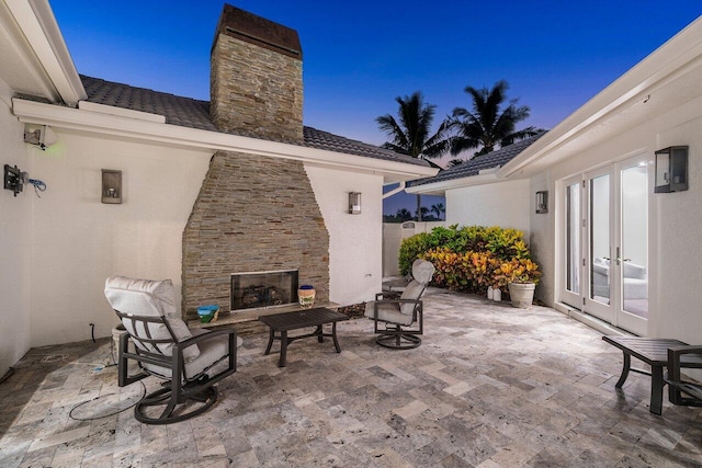 patio terrace at dusk with french doors and an outdoor stone fireplace