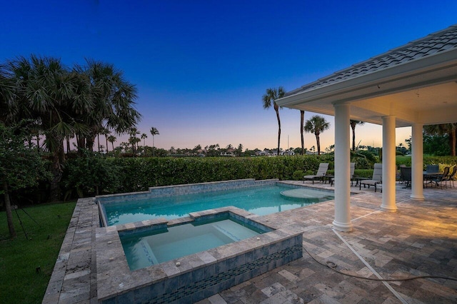 pool at dusk with a patio area and an in ground hot tub