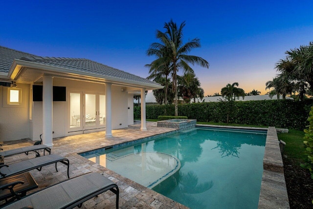 pool at dusk with an in ground hot tub, french doors, and a patio area