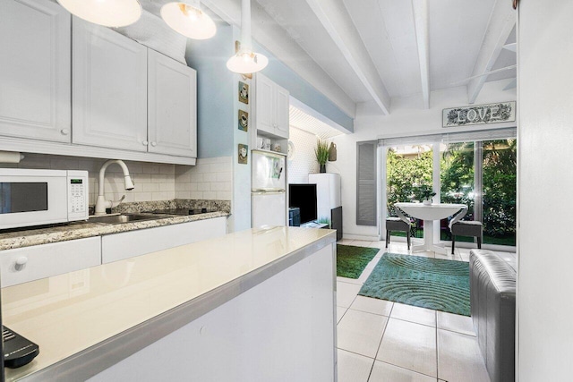 kitchen with beam ceiling, white cabinetry, sink, pendant lighting, and light tile patterned flooring