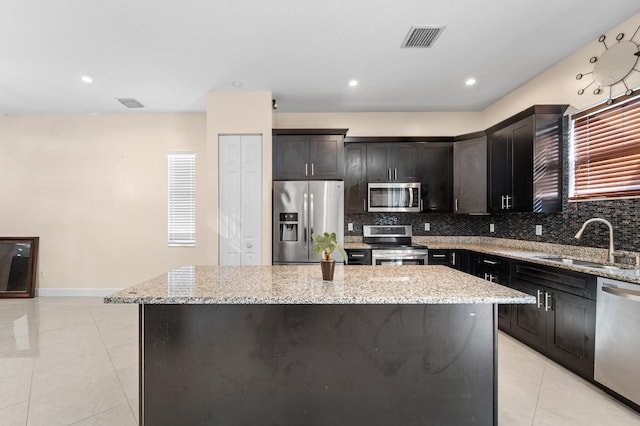 kitchen featuring backsplash, light stone counters, stainless steel appliances, sink, and a center island