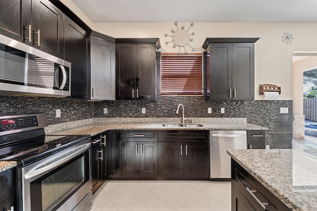 kitchen featuring decorative backsplash, appliances with stainless steel finishes, light stone counters, and sink