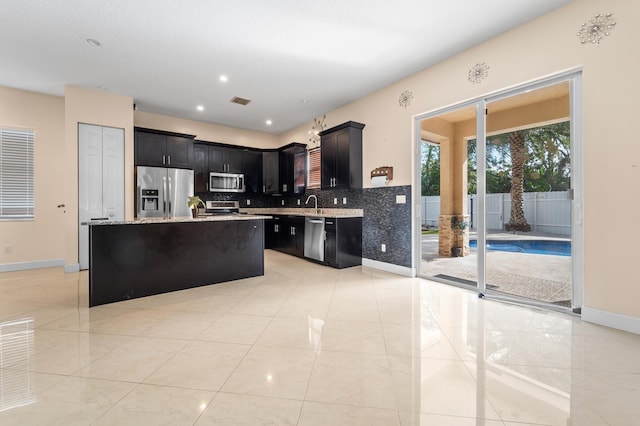 kitchen featuring decorative backsplash, light stone countertops, stainless steel appliances, sink, and a kitchen island