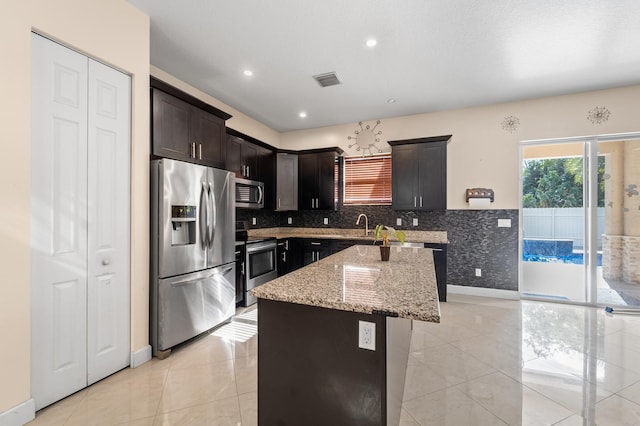 kitchen with backsplash, light stone counters, stainless steel appliances, sink, and a kitchen island