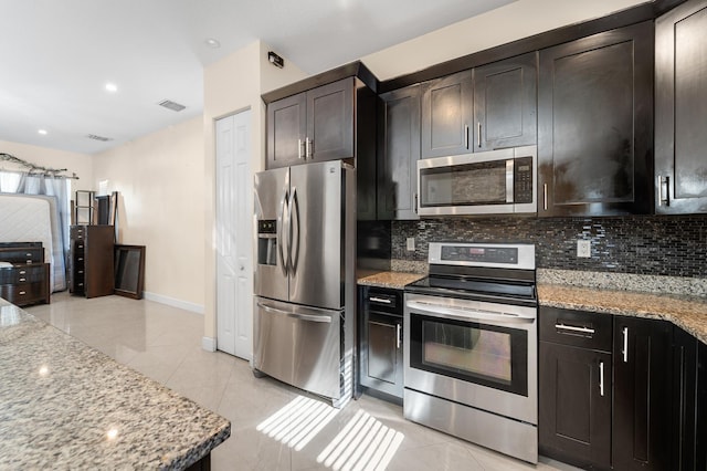 kitchen with appliances with stainless steel finishes, tasteful backsplash, light stone counters, and dark brown cabinets