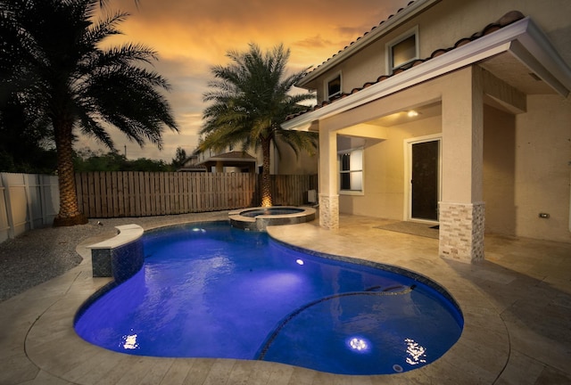 pool at dusk with a patio area and an in ground hot tub