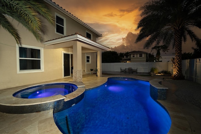 pool at dusk with an in ground hot tub and a patio