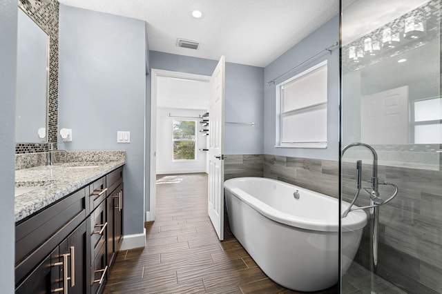 bathroom with a tub to relax in, vanity, and a textured ceiling