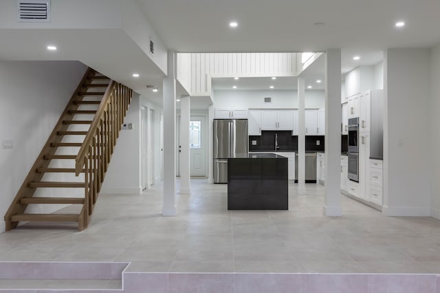 kitchen featuring appliances with stainless steel finishes, a towering ceiling, light tile patterned floors, white cabinets, and a center island