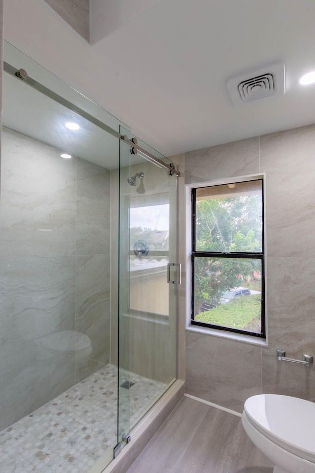 bathroom featuring a shower with shower door, toilet, wood-type flooring, and tile walls