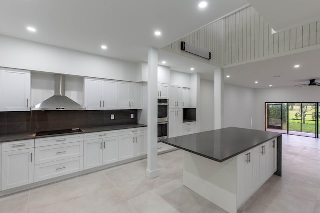 kitchen featuring wall chimney range hood, ceiling fan, black electric cooktop, a kitchen island, and white cabinetry