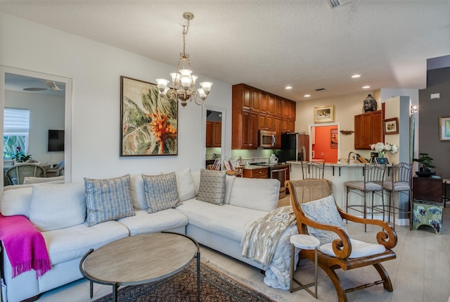 living room featuring ceiling fan with notable chandelier, a textured ceiling, light hardwood / wood-style flooring, and sink