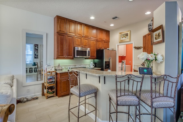 507 Resort Ln, Palm Beach Gardens, FL 33418 - kitchen featuring stainless steel appliances, a breakfast bar, a peninsula, brown cabinetry, and light stone countertops