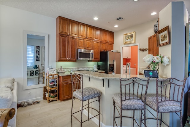 kitchen with kitchen peninsula, light stone countertops, stainless steel appliances, and a breakfast bar