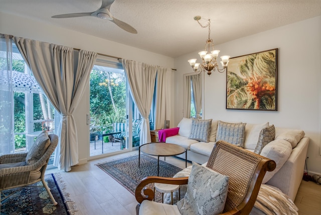 living room featuring ceiling fan with notable chandelier, a textured ceiling, and light wood-type flooring