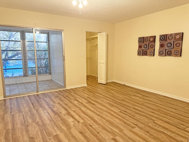 unfurnished bedroom featuring a closet, a spacious closet, a textured ceiling, and light hardwood / wood-style flooring