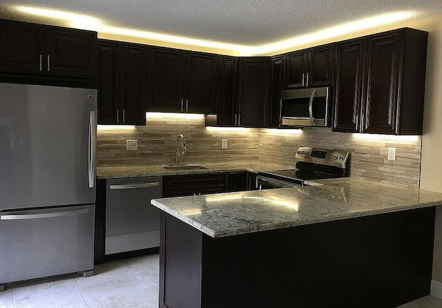 kitchen with decorative backsplash, appliances with stainless steel finishes, light stone countertops, a textured ceiling, and sink