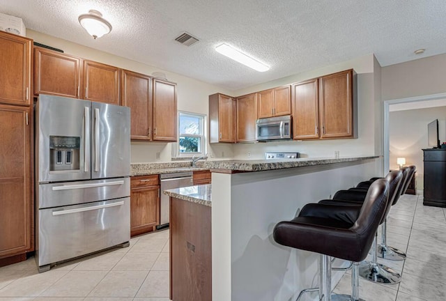 kitchen featuring a breakfast bar area, stone counters, appliances with stainless steel finishes, light tile patterned flooring, and kitchen peninsula