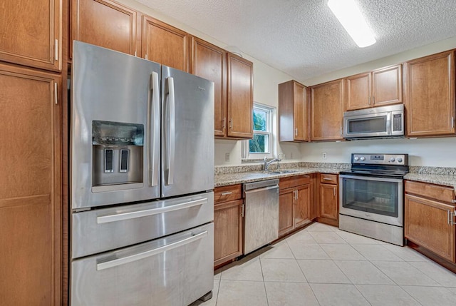 kitchen featuring sink, light stone counters, a textured ceiling, light tile patterned floors, and appliances with stainless steel finishes