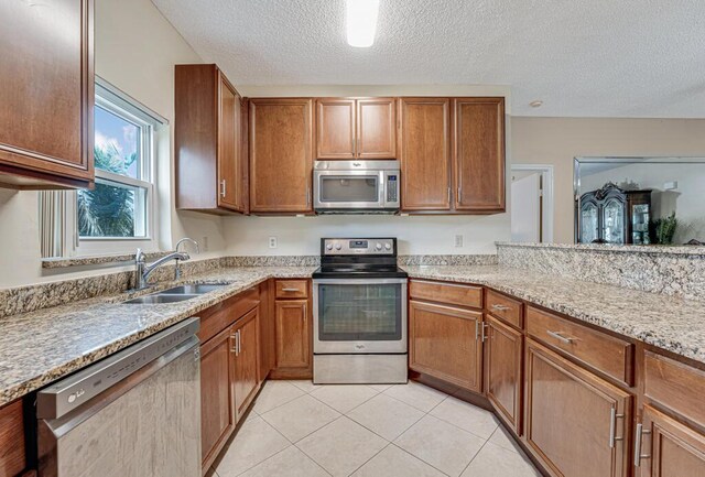 kitchen with light tile patterned flooring, sink, light stone counters, a textured ceiling, and appliances with stainless steel finishes