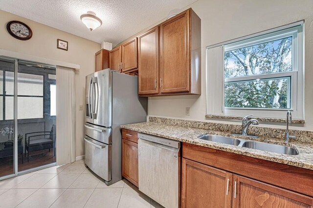 kitchen featuring sink, light tile patterned floors, stainless steel appliances, light stone countertops, and a textured ceiling