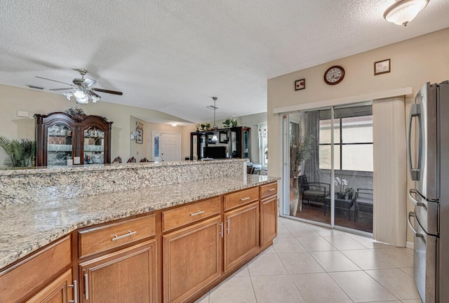 kitchen with light stone counters, a textured ceiling, light tile patterned floors, stainless steel fridge, and ceiling fan