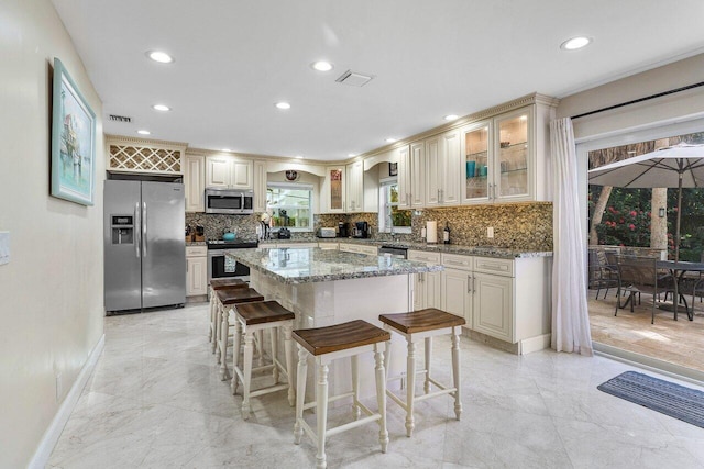 kitchen featuring light stone countertops, appliances with stainless steel finishes, a center island, and tasteful backsplash