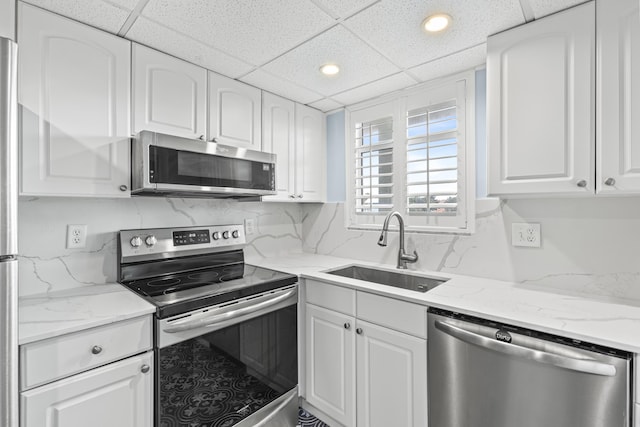 kitchen featuring a paneled ceiling, white cabinets, sink, light stone countertops, and appliances with stainless steel finishes