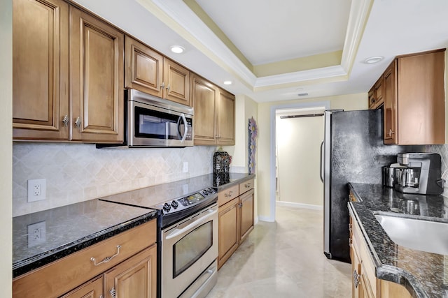 kitchen with appliances with stainless steel finishes, backsplash, ornamental molding, a tray ceiling, and dark stone countertops