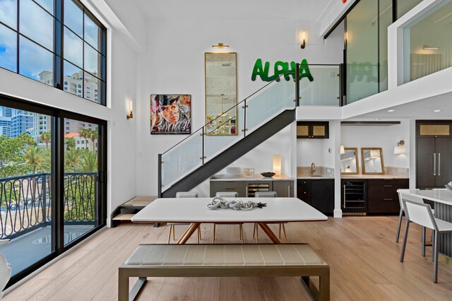 dining space with light wood-type flooring, sink, wine cooler, and a high ceiling