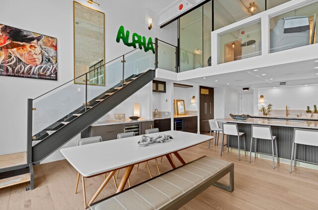 dining space with a towering ceiling, sink, wine cooler, and light hardwood / wood-style flooring