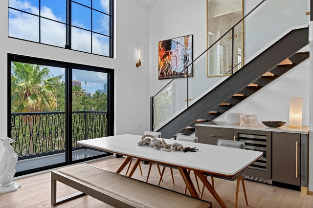 dining space featuring a wealth of natural light, a towering ceiling, light hardwood / wood-style flooring, and beverage cooler