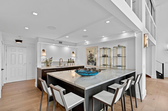 kitchen featuring sink, light hardwood / wood-style flooring, light stone counters, kitchen peninsula, and a breakfast bar area