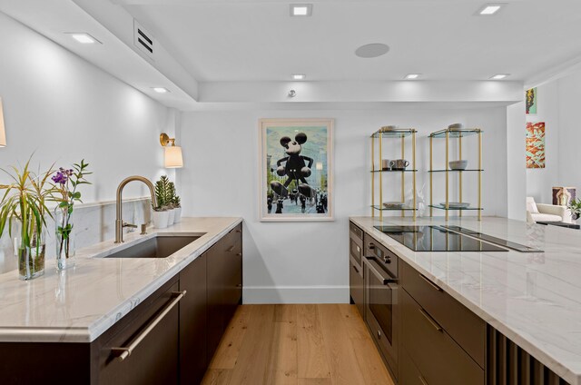 kitchen with sink, light stone counters, oven, black electric stovetop, and light wood-type flooring