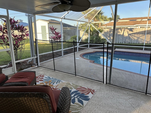 view of pool featuring a lawn, glass enclosure, ceiling fan, a storage unit, and a patio area