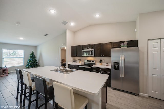 kitchen featuring stainless steel appliances, a kitchen island with sink, sink, light hardwood / wood-style floors, and lofted ceiling