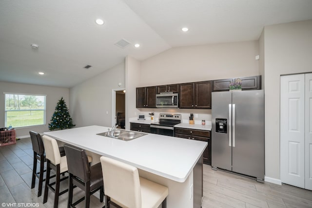 kitchen with sink, an island with sink, vaulted ceiling, a breakfast bar, and appliances with stainless steel finishes