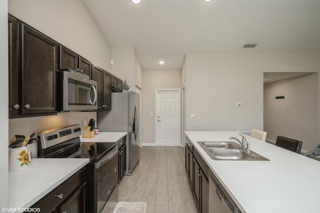 kitchen with sink, light hardwood / wood-style floors, a kitchen bar, dark brown cabinets, and appliances with stainless steel finishes