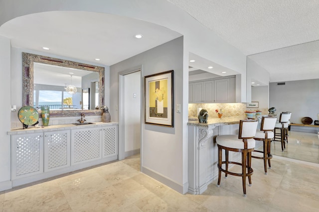 kitchen with kitchen peninsula, a kitchen breakfast bar, backsplash, light stone counters, and a notable chandelier