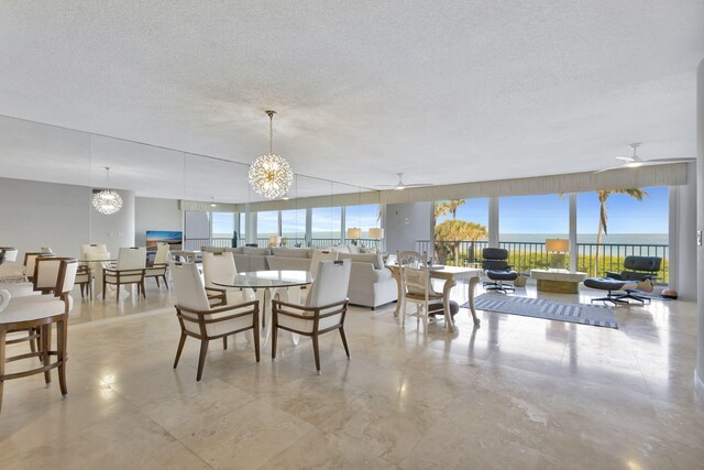 dining area featuring a textured ceiling, a water view, a healthy amount of sunlight, and ceiling fan with notable chandelier