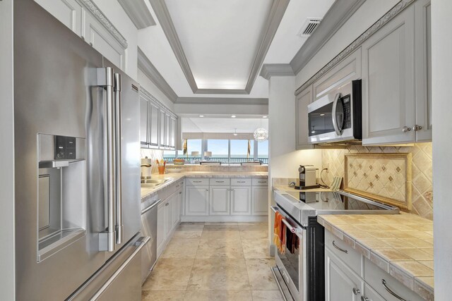 kitchen featuring crown molding, a raised ceiling, backsplash, and appliances with stainless steel finishes