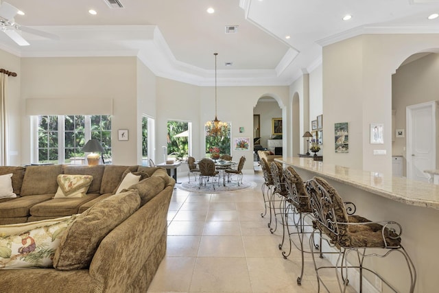 tiled living room with a towering ceiling, ceiling fan with notable chandelier, a raised ceiling, and ornamental molding