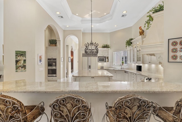 kitchen featuring ornamental molding, custom range hood, appliances with stainless steel finishes, light stone counters, and kitchen peninsula