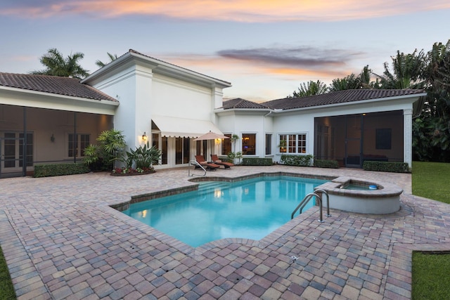 pool at dusk with an in ground hot tub and a patio